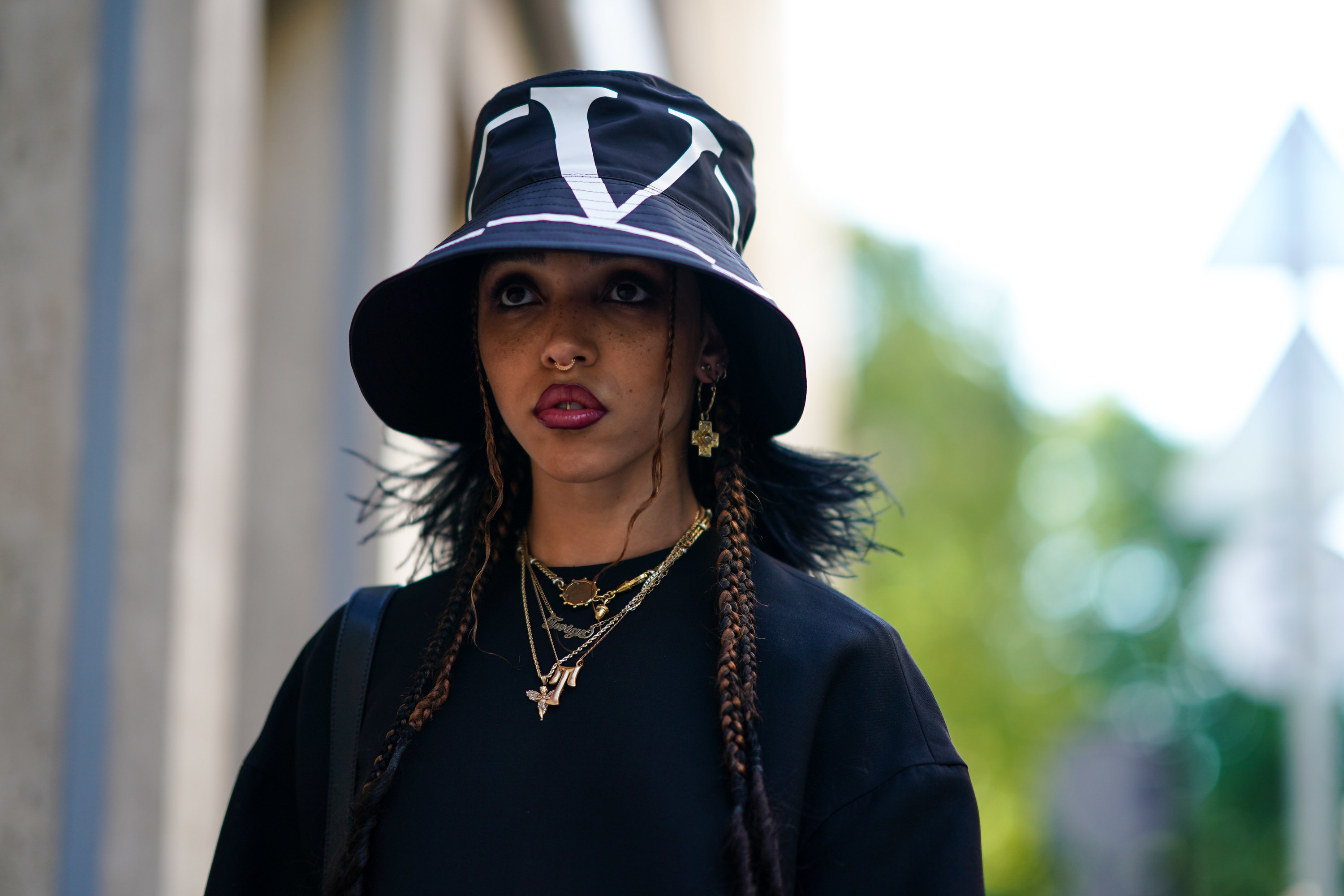 FKA Twigs wears a Valentino hat, a black dress, necklace, earrings, outside Valentino, during Paris Fashion Week 