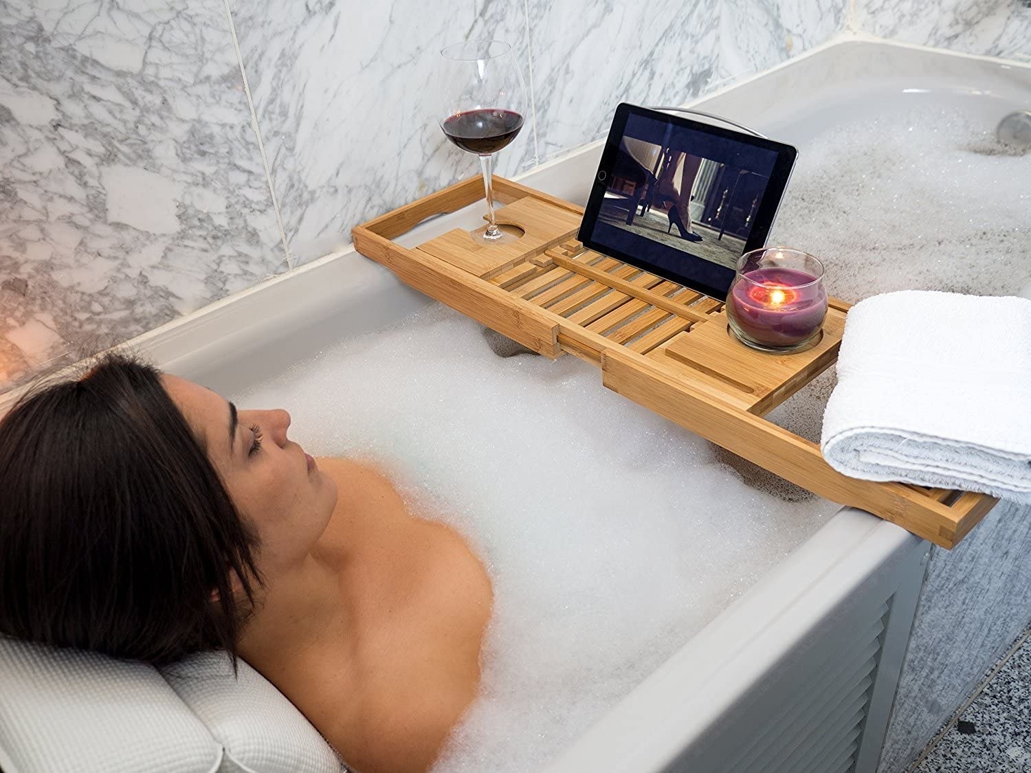 A person lounging in a bubble bath while watching something on a tablet that is sitting on the bathtub tray 