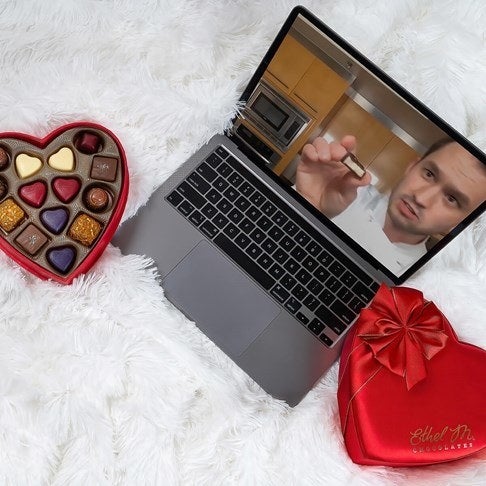 Heart-shaped box of chocolates next to laptop with virtual class on screen