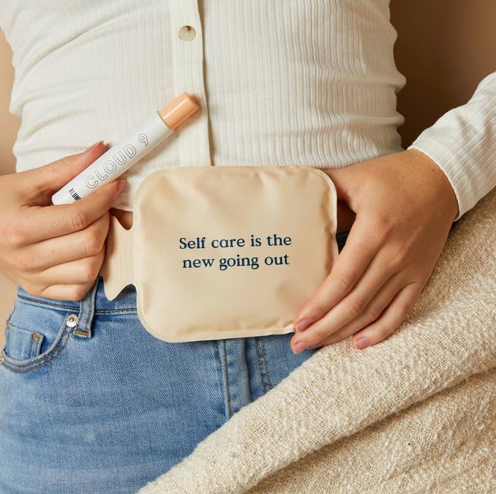 person holding heating pad on their stomach in one hand and the oil in the other hand