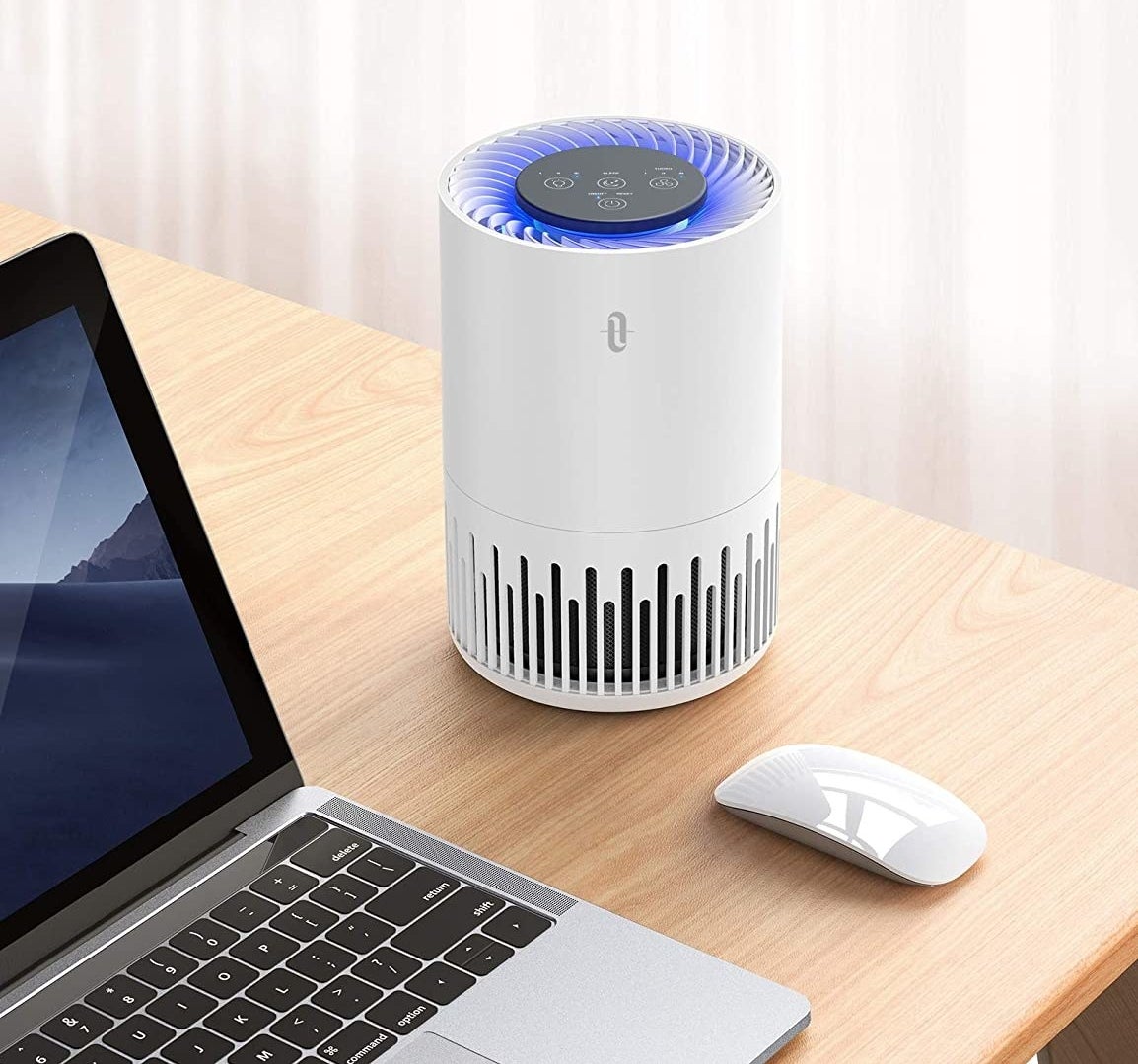 The air purifier on a desk next to a laptop