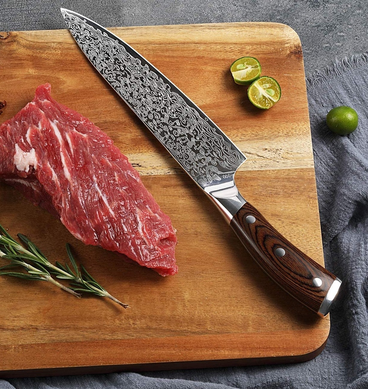 A knife on a cutting board next to a lime, steak, and rosemary 