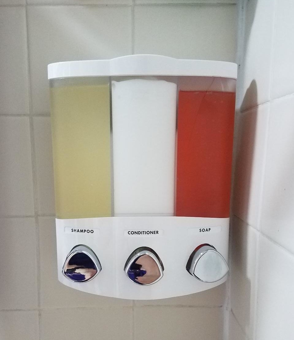  A reviewer&#x27;s photo of the soap dispenser with labels for shampoo, conditioner, and soap
