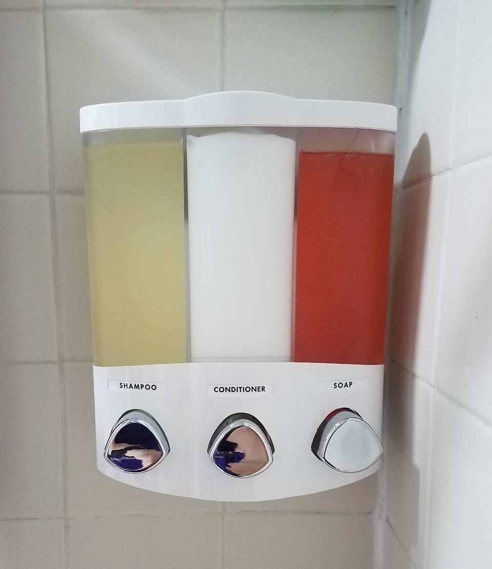 A reviewer's photo of the soap dispenser with labels for shampoo, conditioner, and soap
