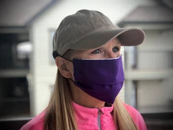 A model in a gray baseball cap with buttons on either side of it hooking a face mask in place 