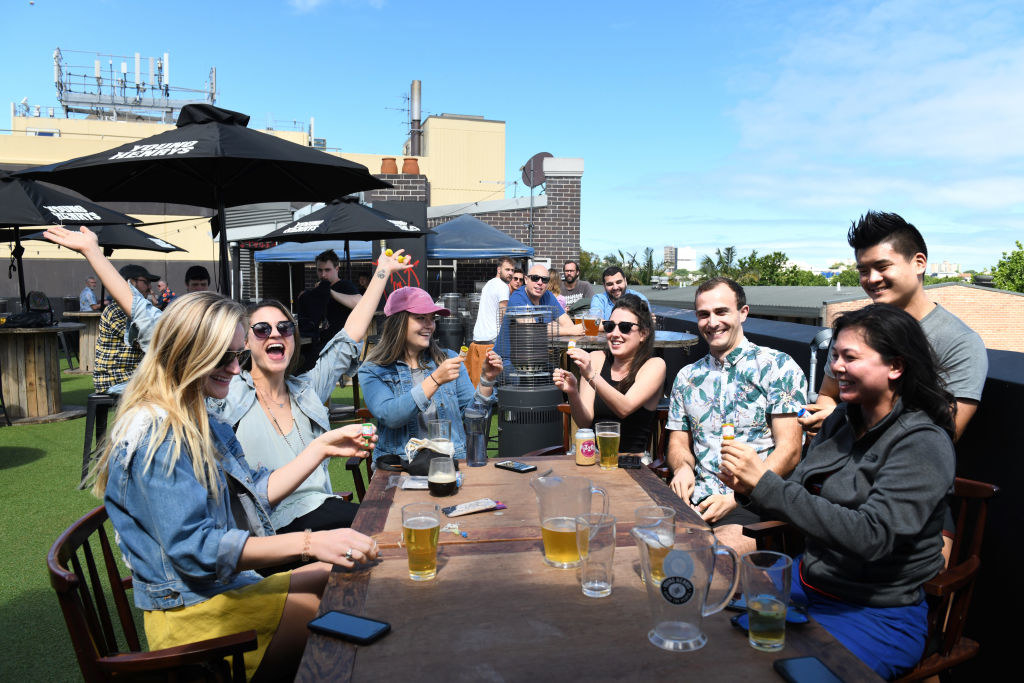 Several people sitting around an outdoor table smiling and drinking beer without a care in the world