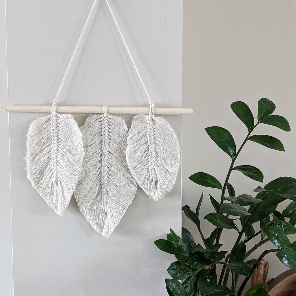 The leaf-patterned macrame hanging on a wall next to a plant