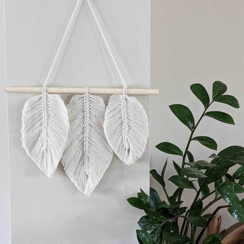 The leaf-patterned macrame hanging on a wall next to a plant 