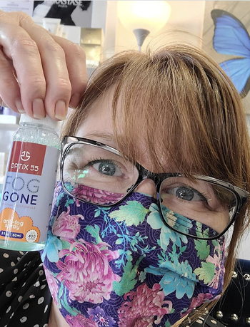 Reviewer holding up bottle of spray with unfogged glasses and face mask on 