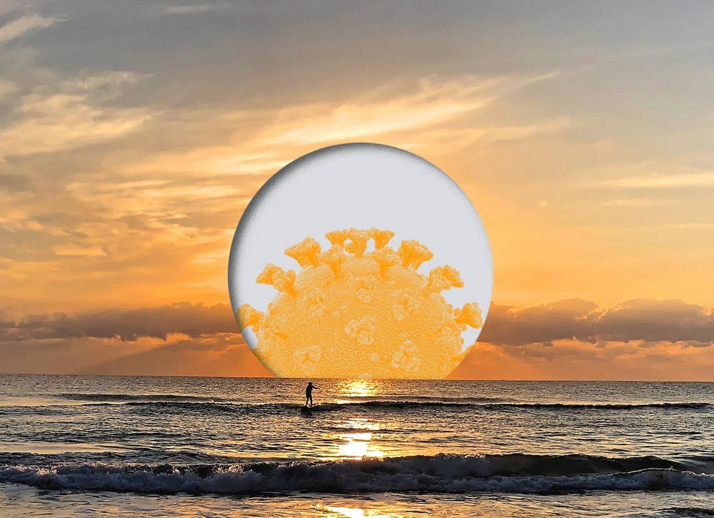 A surfer rides a wave as the sun, illustrated with a coronavirus germ, sets behind them