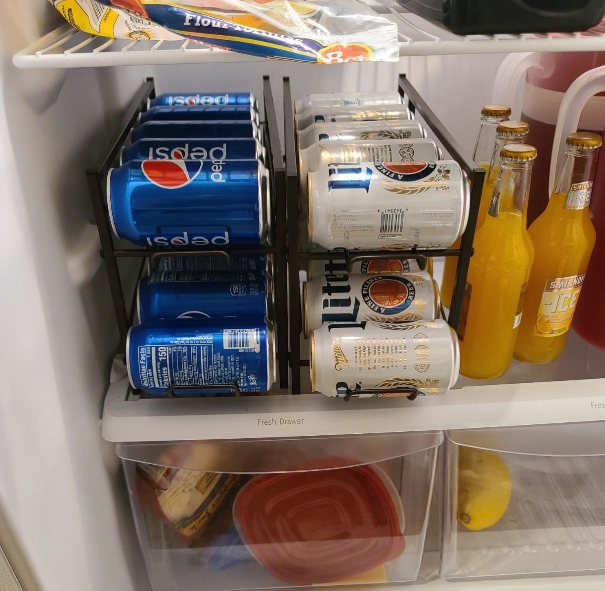 reviewer image of soda and beer cans organized on two soda can racks in a customer&#x27;s fridge
