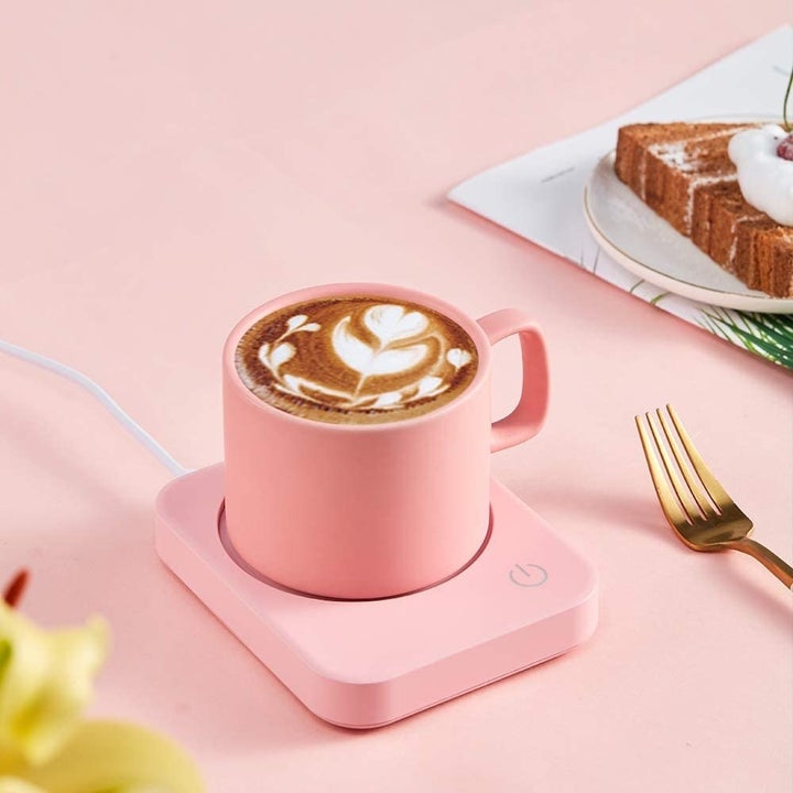 A pink mug warmer on a desk with a mug onf coffee on it 