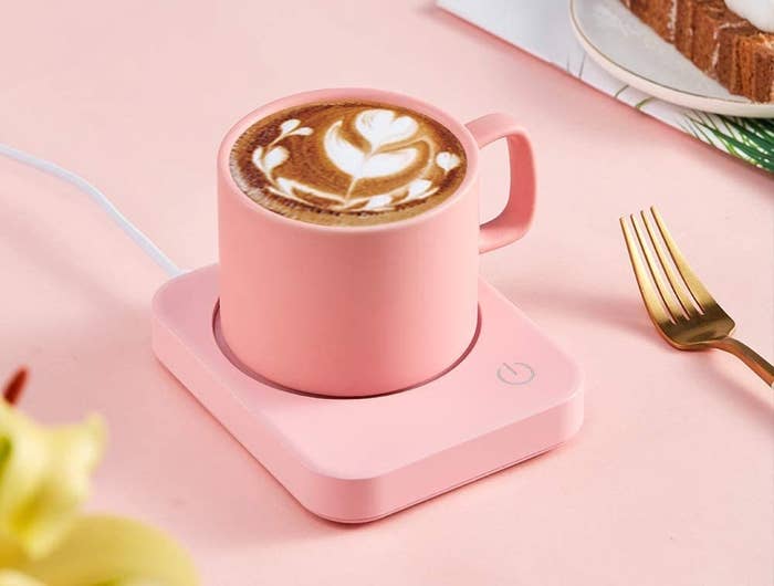 A pink mug warmer on a desk with a mug of coffee on it