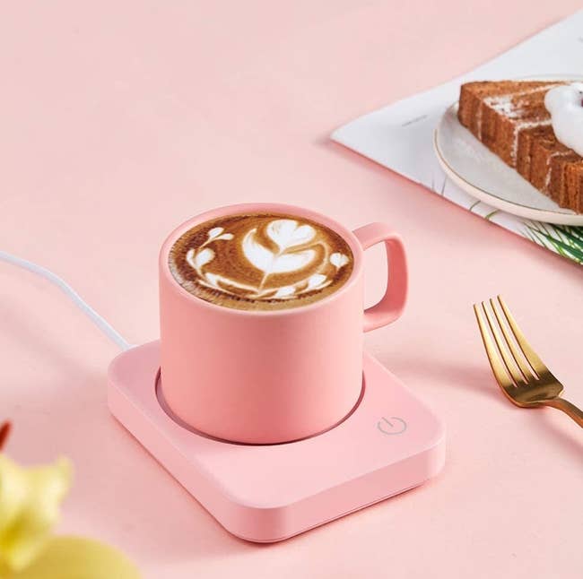A pink mug warmer on a desk with a mug of coffee on it 