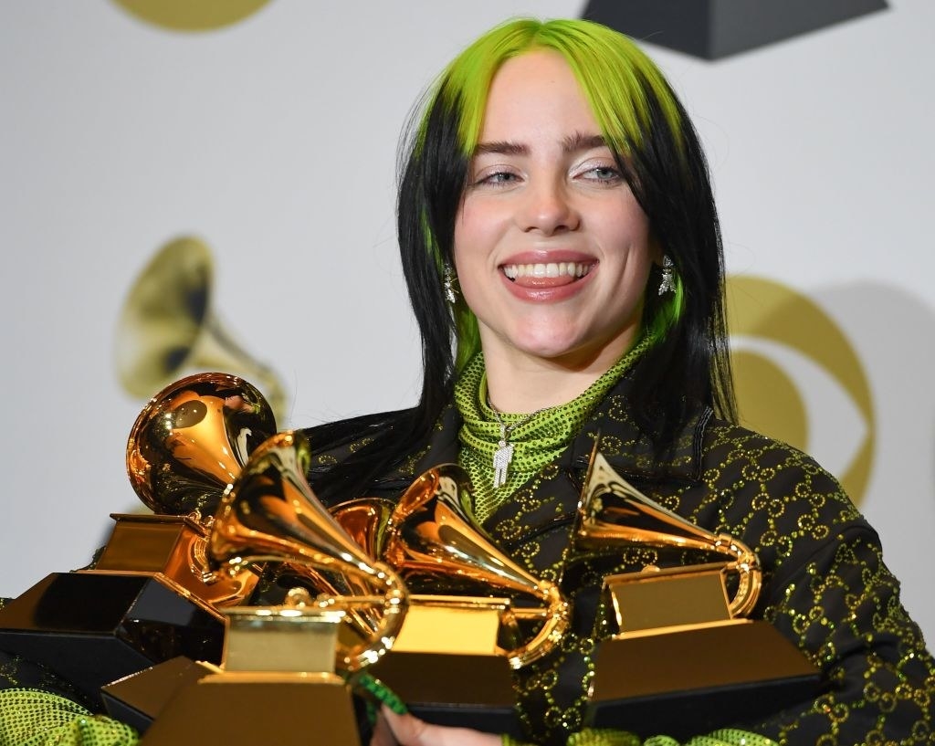 Billie smiling and holding her five Grammys back stage