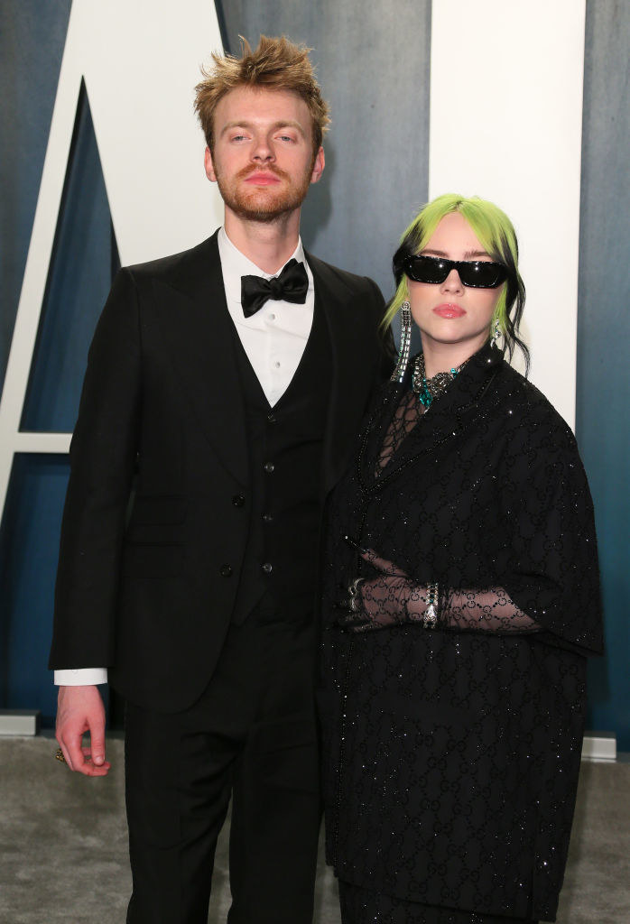 Finneas and Billie, wearing sunglasses, posing on a red carpet with their arms around each other