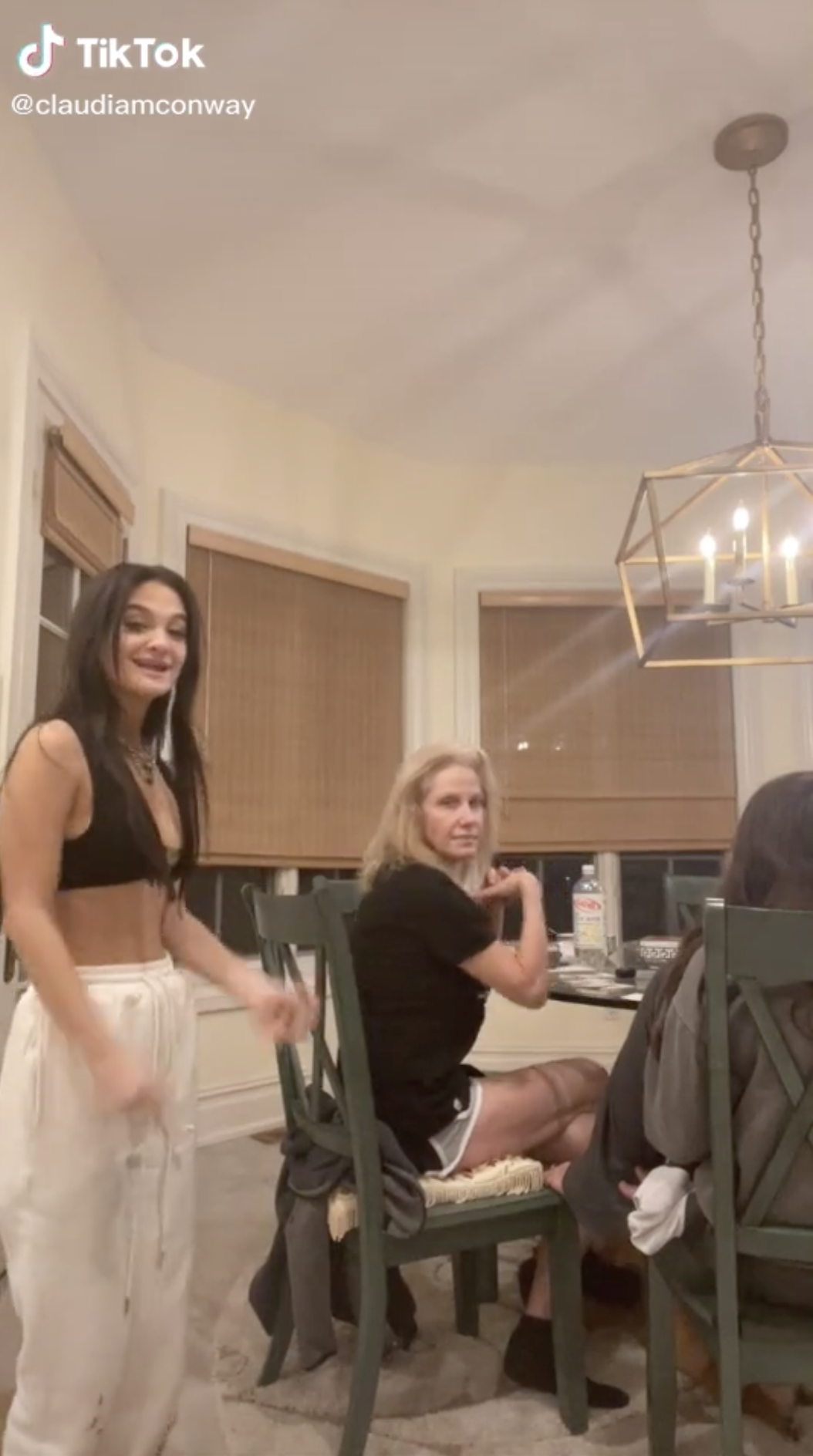 Screenshot from Claudia&#x27;s TikTok showing Kellyanne sitting at a table in a T-shirt and shorts and Claudia standing behind her
