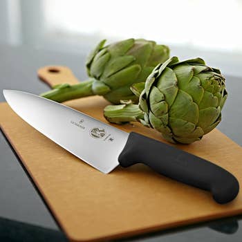 A stainless steel knife with a black handle sitting on a cutting board 