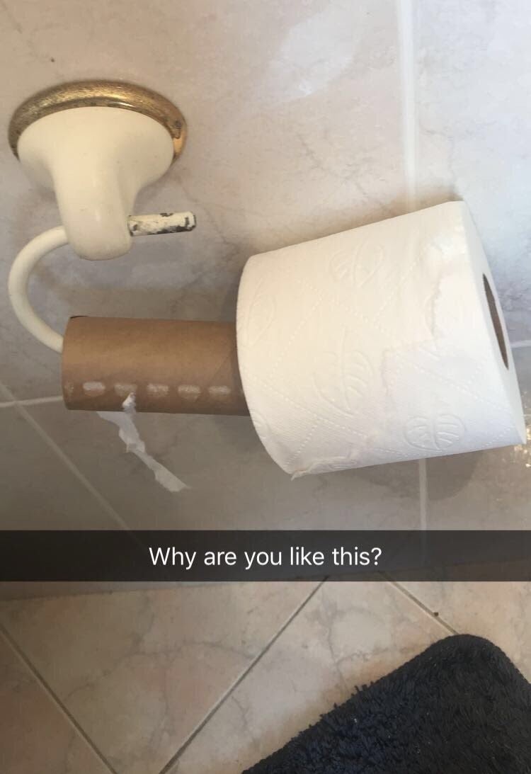 A new roll of toilet paper partially hanging off the roll on top of the old empty roll