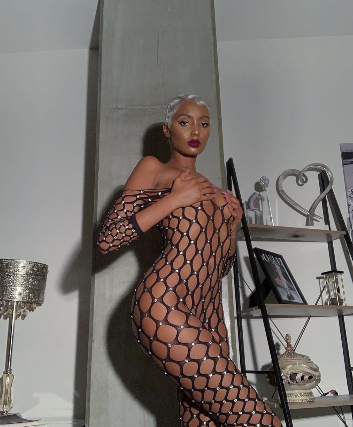 a model in a black fish net off the shoulder jump suit with an array of crystals on it