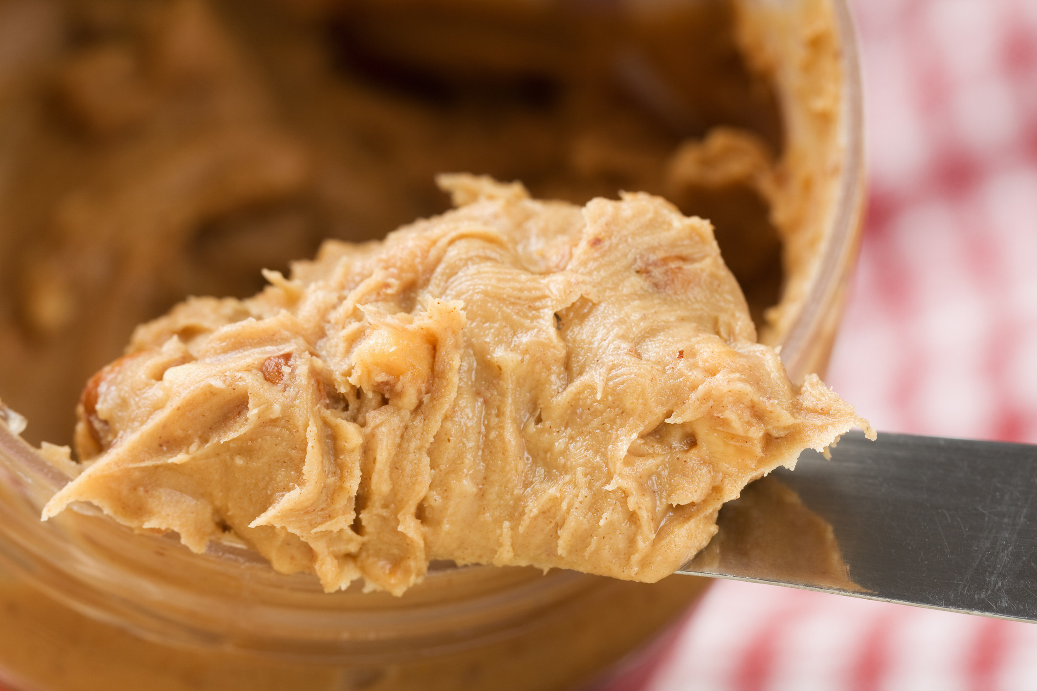 A heap of crunchy peanut butter on a knife coming out of the jar