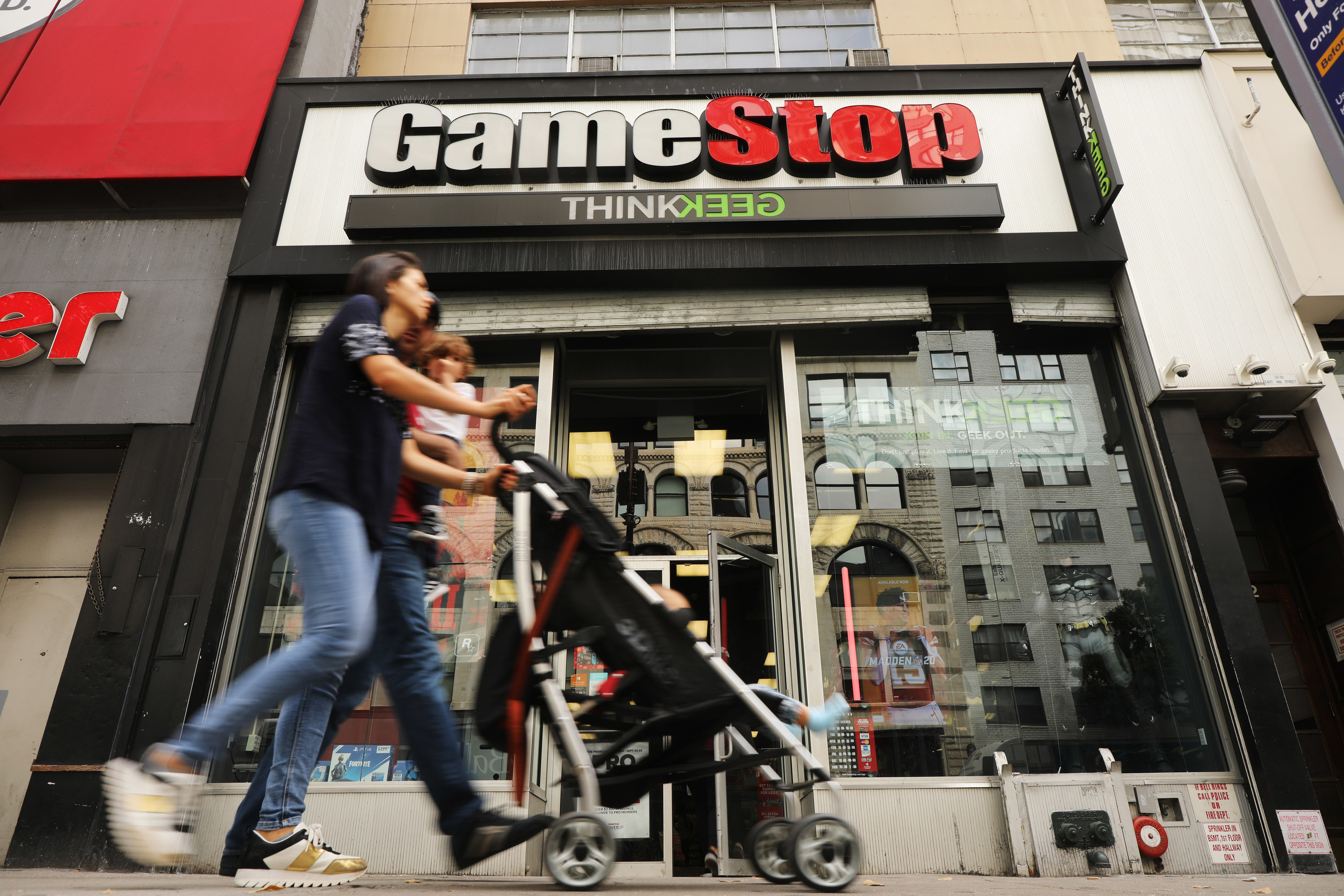 A couple pushing a stroller walk past a GameStop store