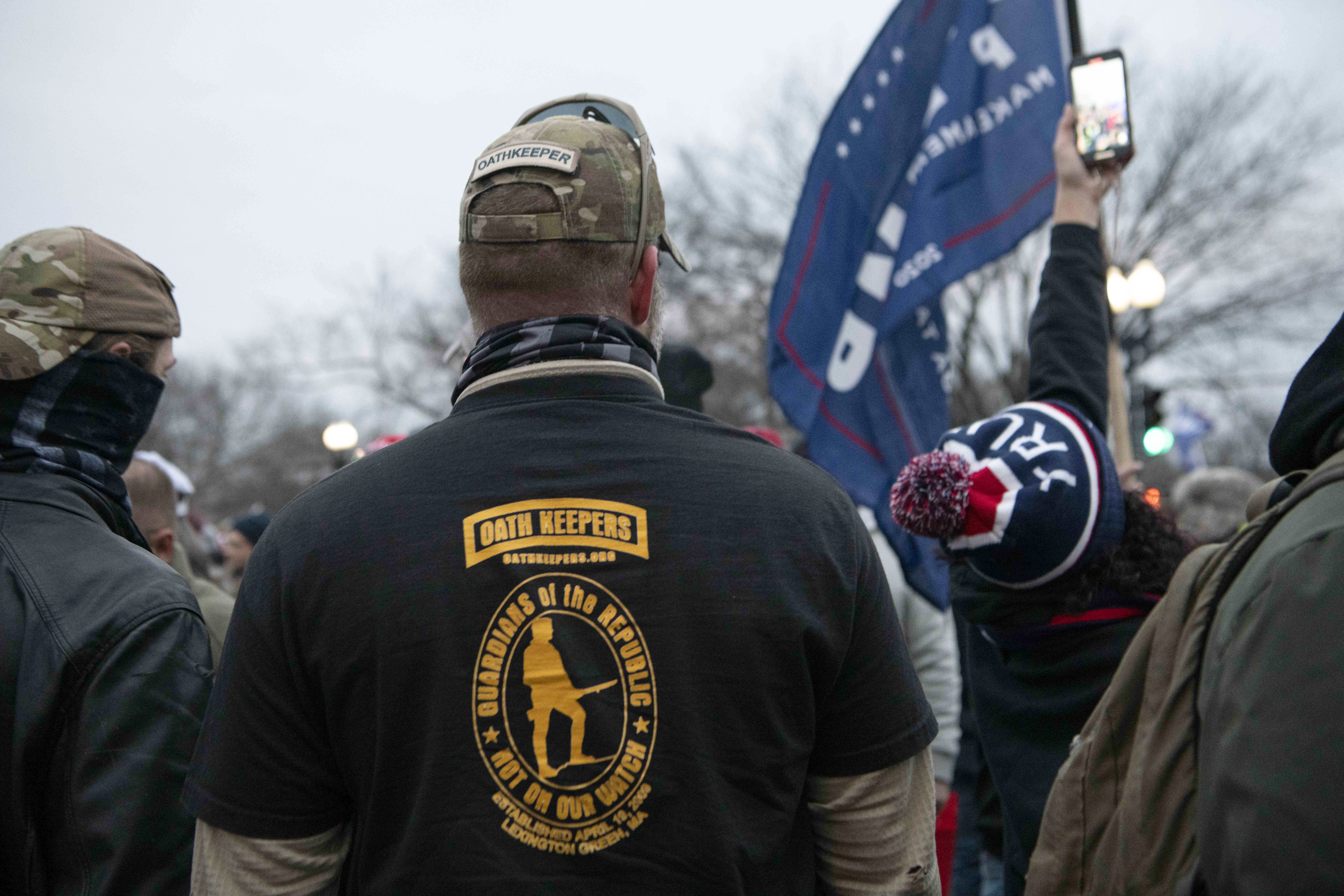 A man with his back to the camera wears a T-shirt that reads &quot;Oath Keepers: Guardians of the Republic — Not on Our Watch&quot;