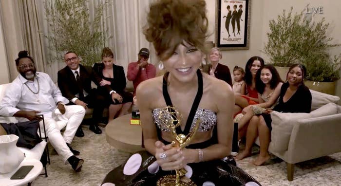 Zendaya, at home, holding her Emmy while wearing a two piece rhinestone and polka dot gown. 
