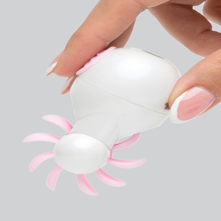 Hand holding the palm-sized toy with a while of tongue-like attachments in white