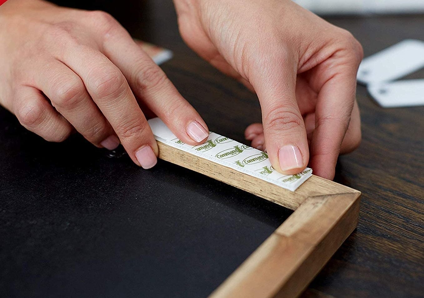 person sticking a command strip on a frame