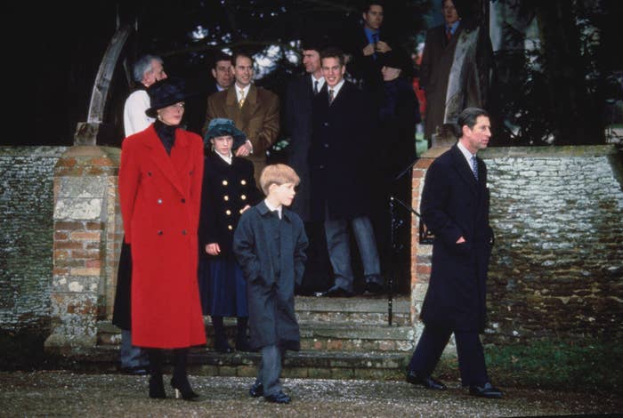 Princess Diana, wearing a long winter coat and hat, walks with a young Prince Harry and Prince Charles