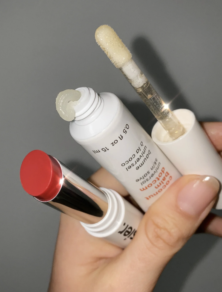 a model holding a red lipstick, a tube of lip balm, a lip gloss applicator