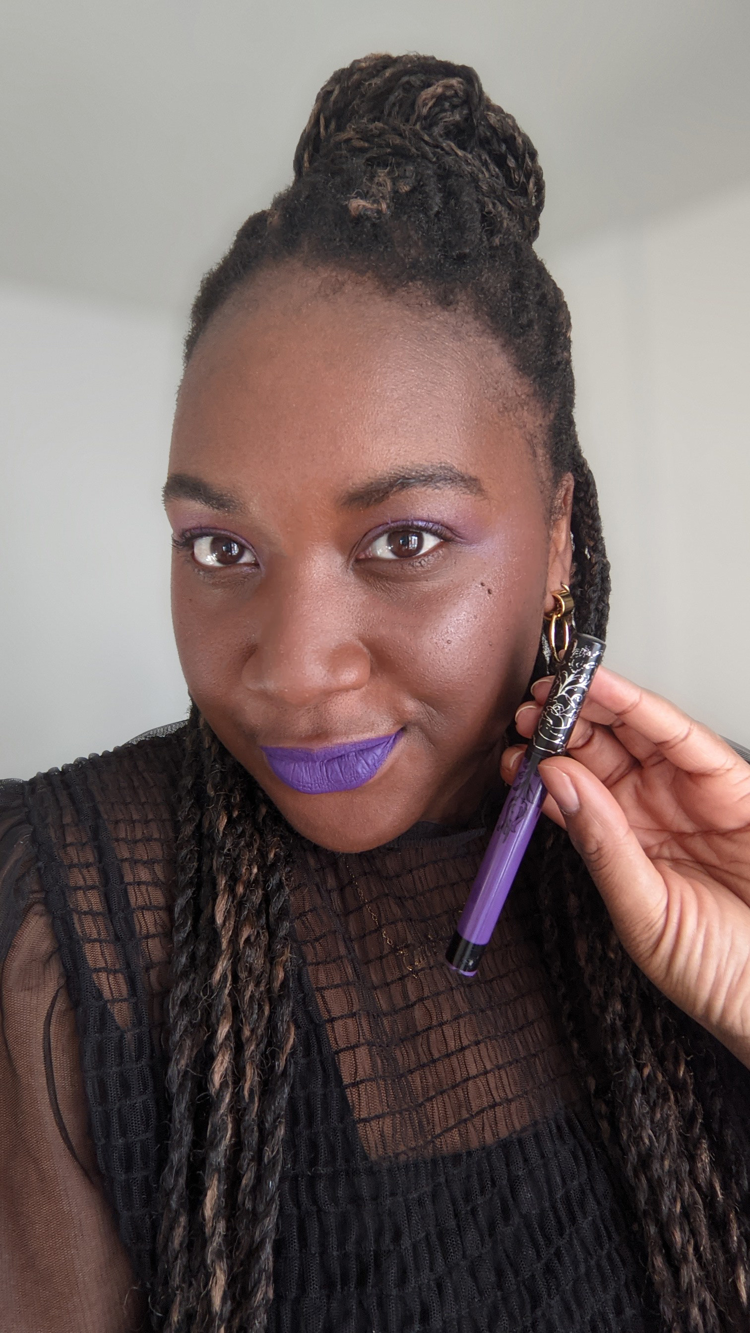 A person wearing bright lipstick and holding a tube of liquid lipstick in their hand