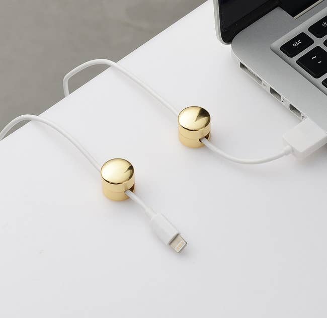 A set of two gold finished round cable organizers installed on a desk with a charger wire running through them 