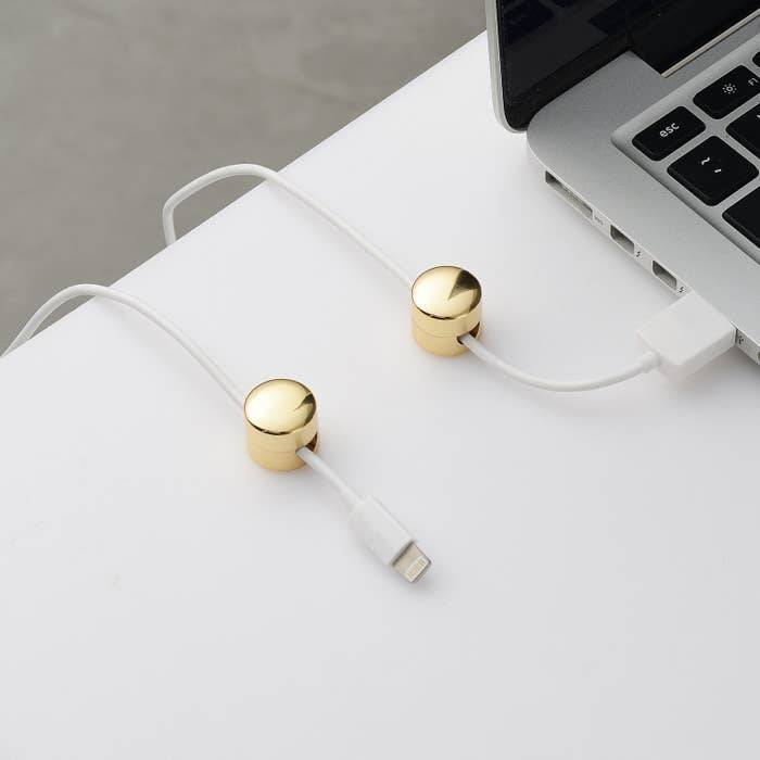 A set of two gold finished round cable organizers installed on a desk with a charger wire running through them 