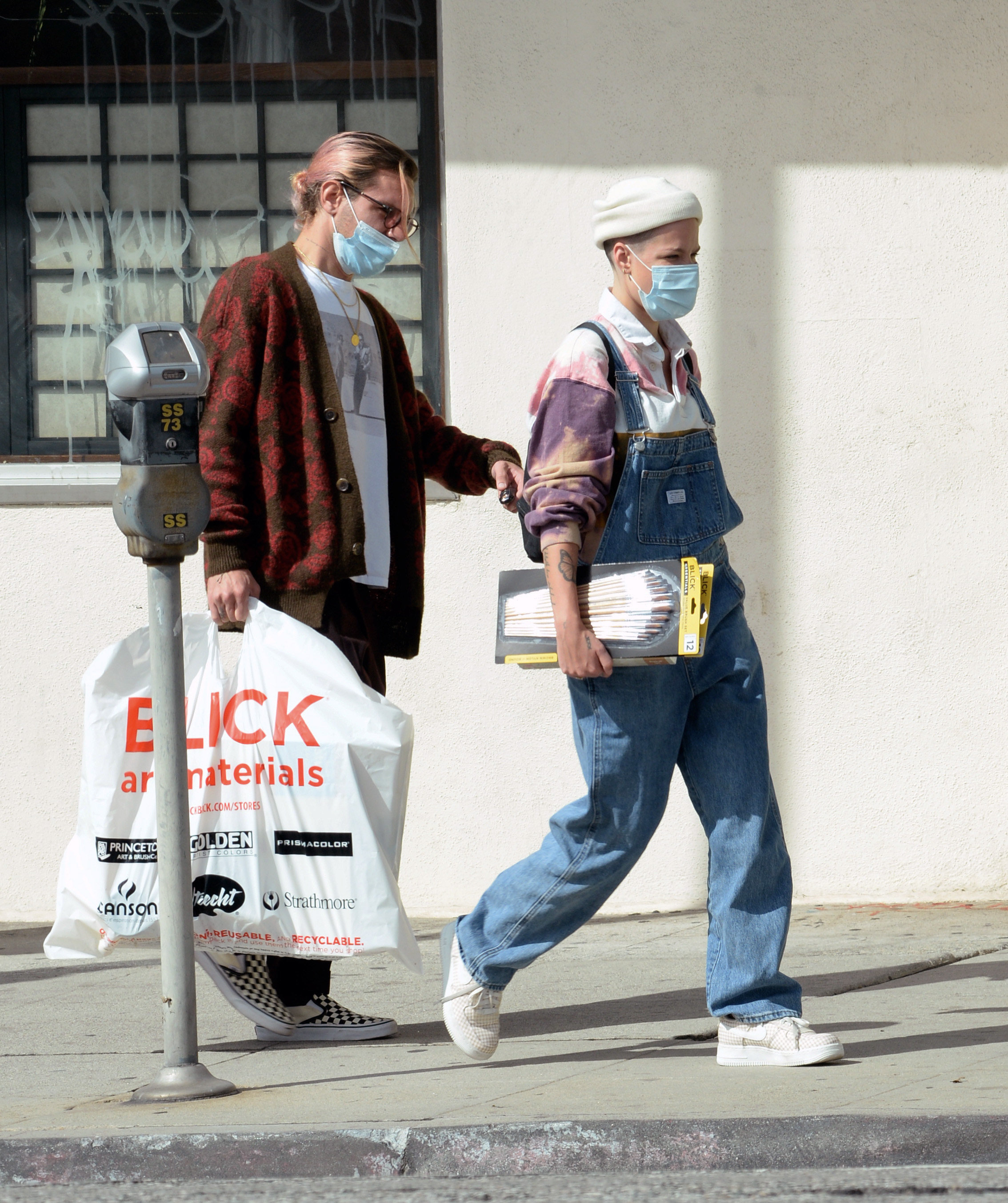 Halsey and Alev walking with items they purchased while casually dressed and wearing face masks