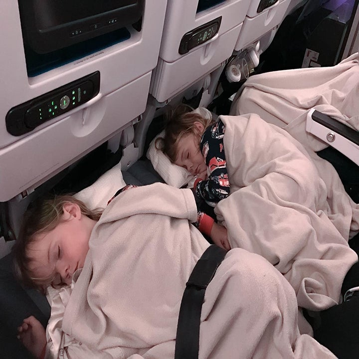 Two kids sleeping with their heads on the footrest in an airplane.