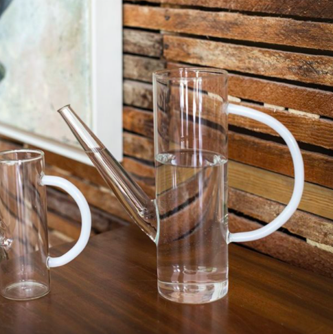A tall sculptural glass watering can with a large frosted handle