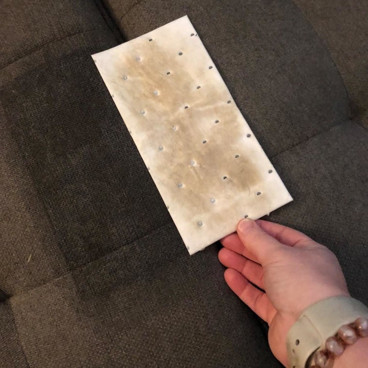 A reviewer photo of a hand holding a pet lifting pad that's stained with brown 