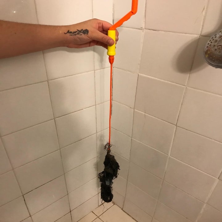 A reviewer photo of a hand holding the drain snake by the handle with a glob of hair on the end