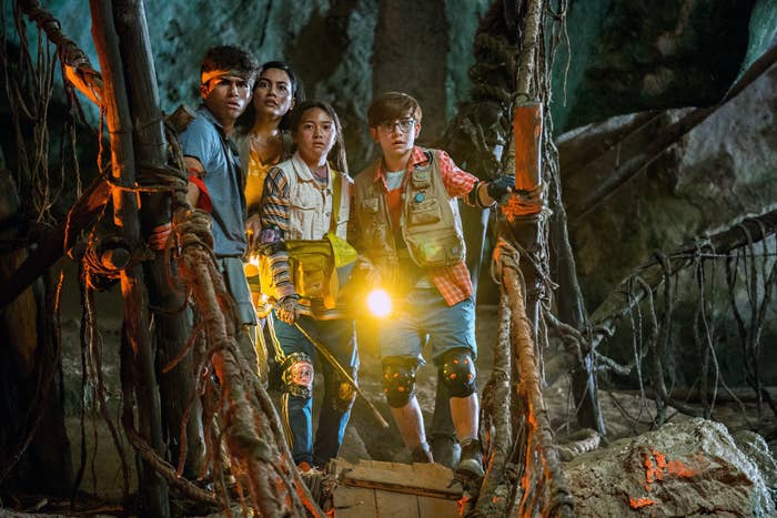 Four kids stand at the edge of an old rope bridge inside a cave