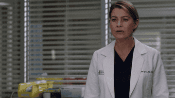 Ellen Pompeo as Meredith Grey, wearing a white lab coat and looking concerned