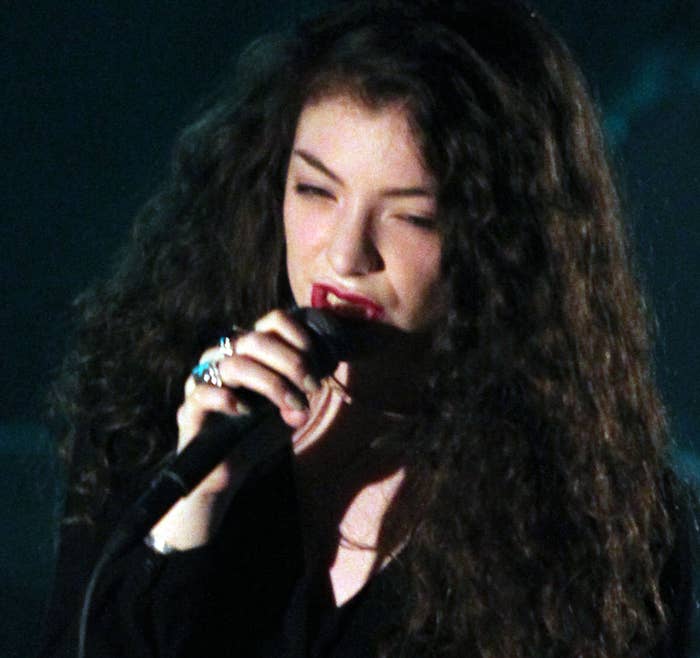 A woman with dark hair and wearing several rings sings into a microphone 