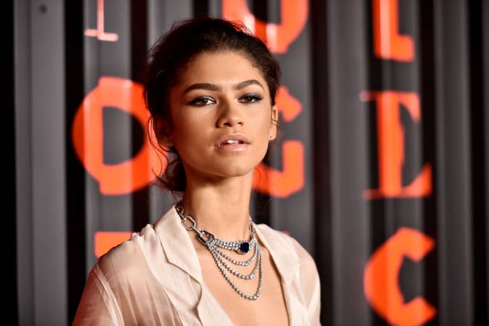 Zendaya from the shoulders up in front of a curtain with indistinct text on it