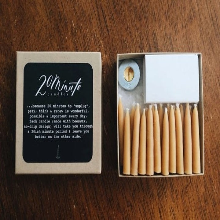 A box An open box filled with small beeswax taper candles, a brass stand, and a box of matches with a lid that says "20 Minute Candles" 
