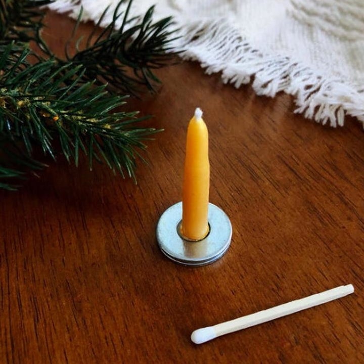 A closeup of a small beeswax taper candle on a brass stand next to a single match 