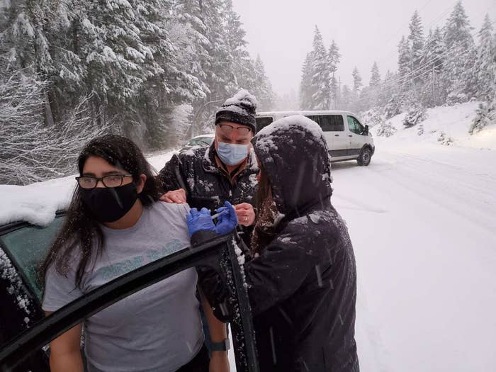 Two people inject a woman with a vaccine on a snowy road