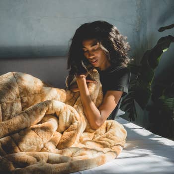 Model snuggling a honey brown faux fur weighted blanket 