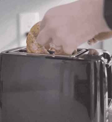 An animated GIF of a person putting a bagel into a black toaster.