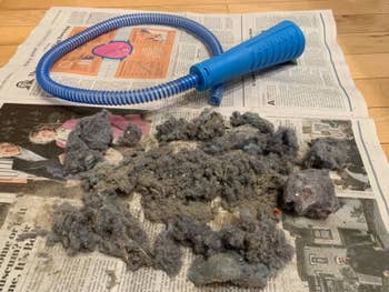 A reviewer's vacuum attachment sitting on a laid-out newspaper next to a large pile of dust 